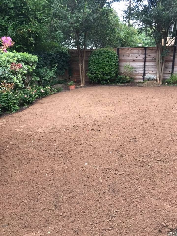 Backyard with prepared bare soil beside a wood fence and established plants