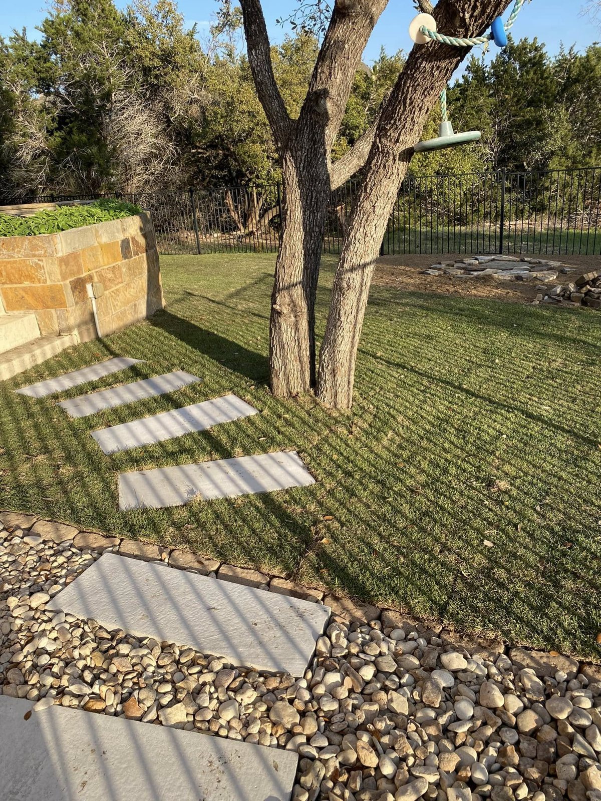 Stone stepping path, river rock border, and lawn around a mature tree