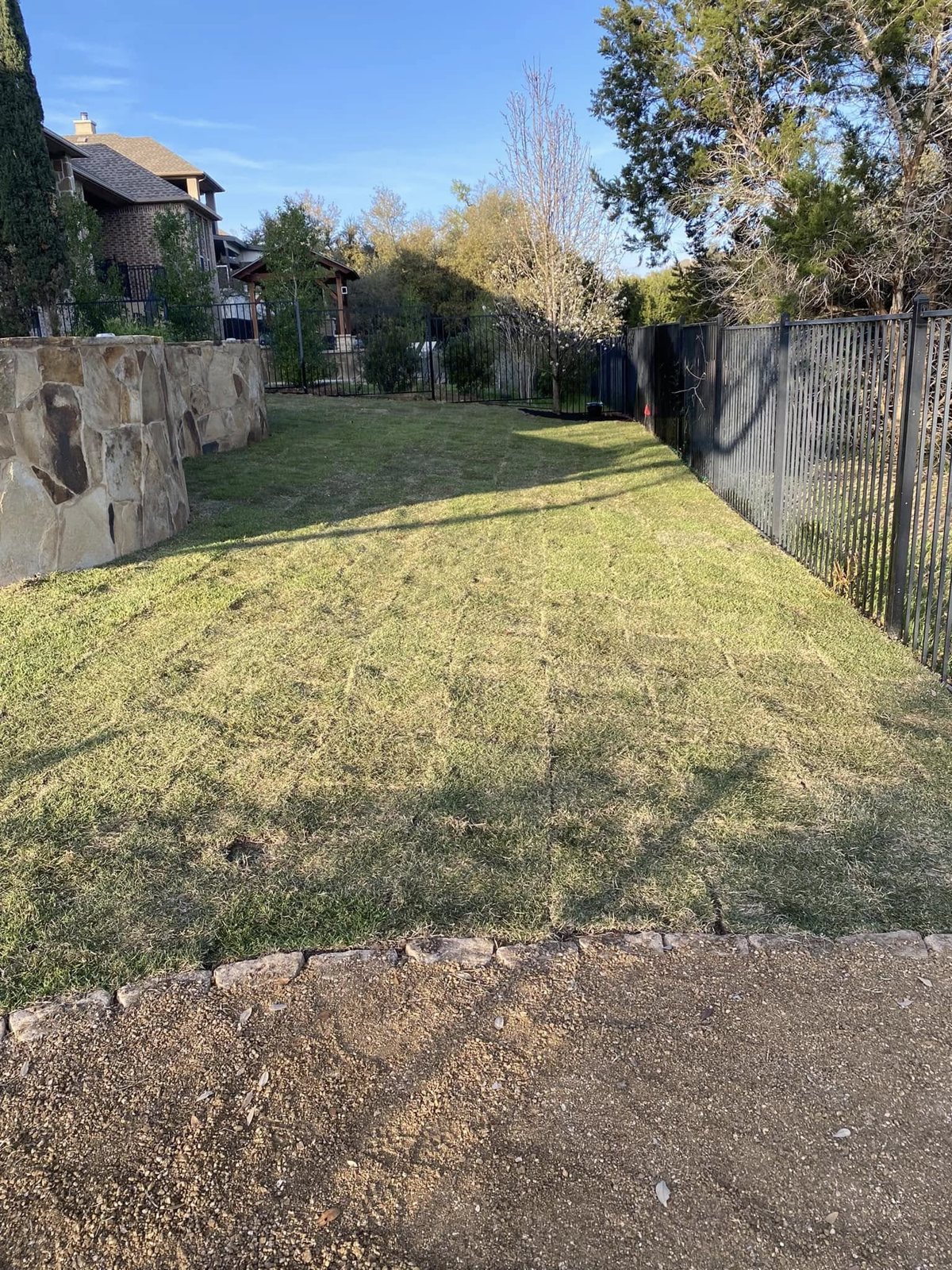Natural grass lawn alongside a stone wall and iron fence